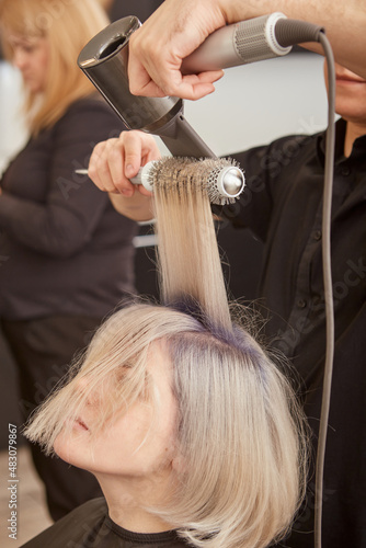 Hairdresser styling client hair with hairdryer and round brush