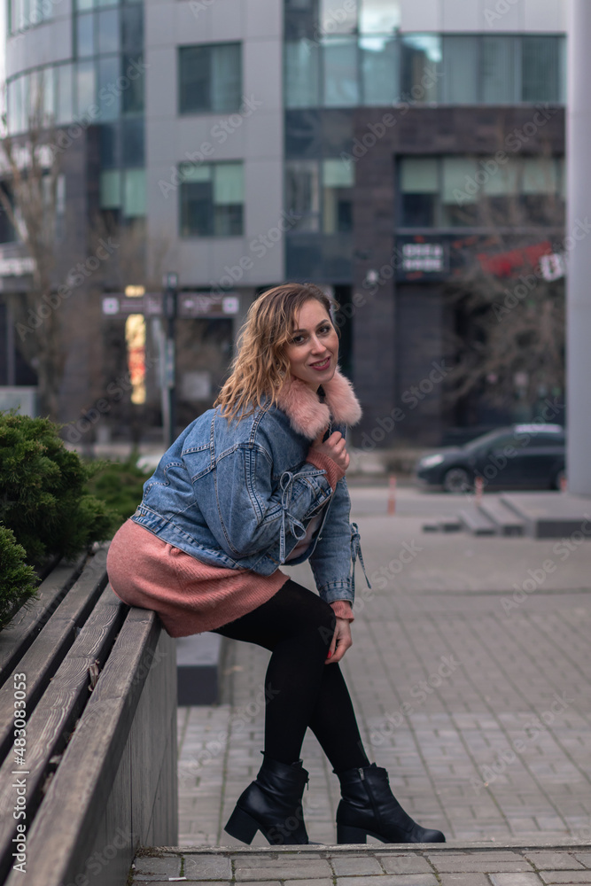 Fototapeta premium young sexy woman sits on a bench in the city against the backdrop of an office building