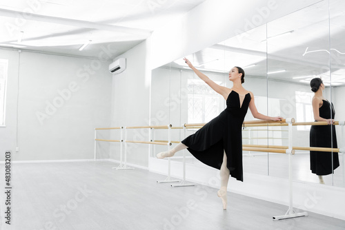 graceful woman in black dress rehearsing near mirrors in ballet studio