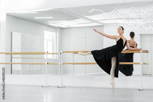 young ballerina in black dress rehearsing at barre near mirrors