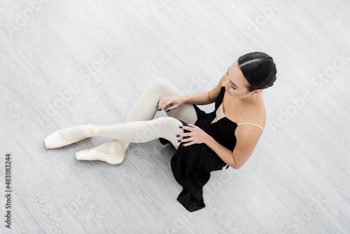 overhead view of young ballerina in black dress sitting on floor in studio