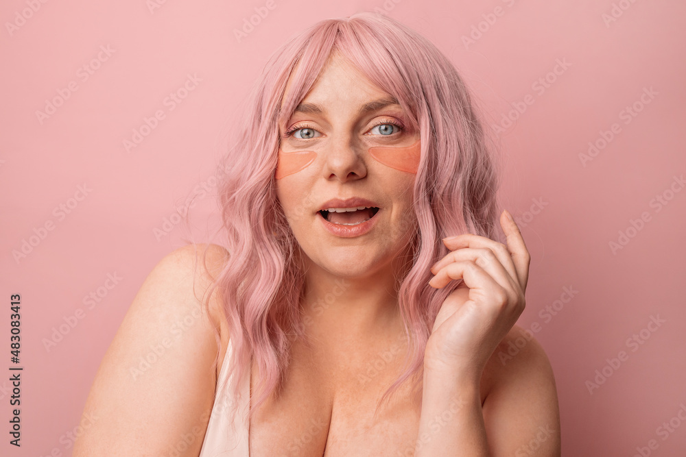 Beautiful woman applying pink under eye patches for dark-circles and puffiness looking at the camera isolated over pink background. Spa, skincare Beautiful woman applying pink under eye patches for dark-circles and puffiness looking at the camera isolated over pink background. Spa, skincare