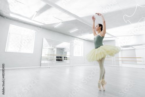 full length view of ballerina in tutu dancing with raised hands in spacious studio