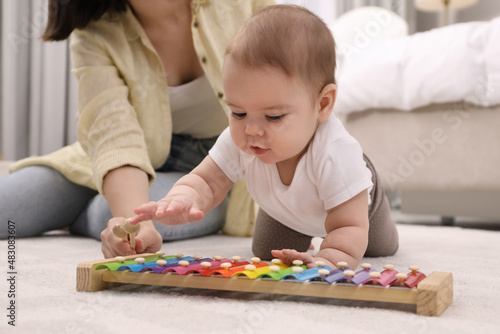 Cute baby and mother playing with xylophone on floor at home