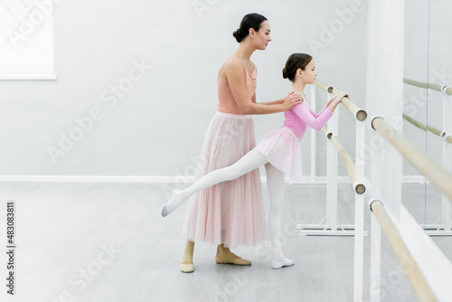 side view of child exercising at barre near graceful ballet teacher photo