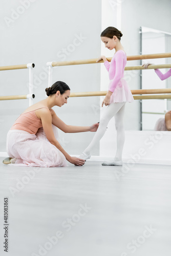 side view of dance teacher touching leg of girl training in ballet school