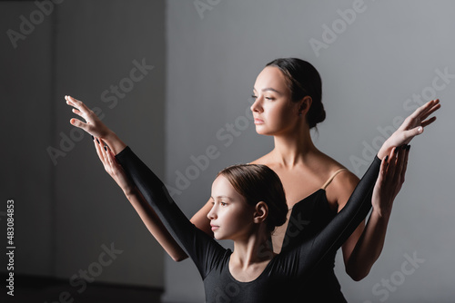 young ballet teacher raising hands of girl during dance lesson photo