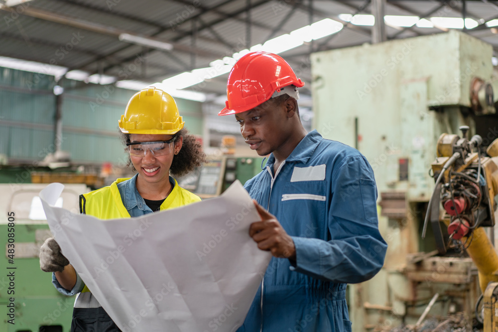 Female and male engineers in safety vest with helmet looking machine drawing for repair and maintenance  cnc machine in  Industry Manufacturing Factory