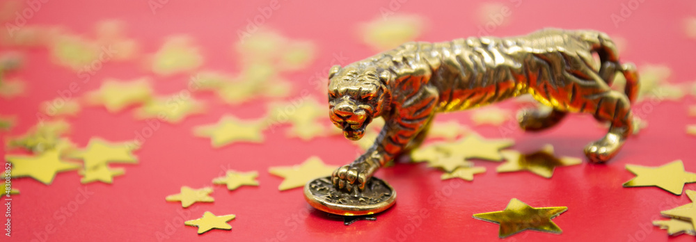 Banner with bronze figure of a tiger with coin - symbol of business on a red background, gold and silver stars copy space. Wishes of good luck, financial well-being and wealth Banner with bronze figure of a tiger with coin - symbol of business on a red background, gold and silver stars copy space. Wishes of good luck, financial well-being and wealth