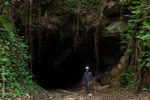 A male speleologist with a helmet exiting the dark cave after studying it