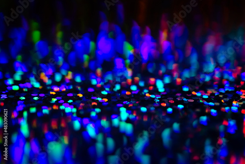 Neon rainbow glittering lights with glow effect abstract background. Defocused festive twinkle lights bokeh. Modern purple, blue, pink, green dark 80s, 90s design