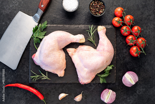 two raw chicken legs with spices and herbs on a stone background
