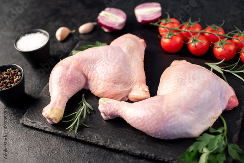 two raw chicken legs with spices and herbs on a stone background