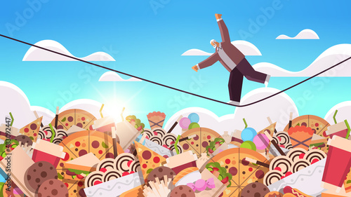 senior man balancing on rope above junk food assortment of fast food unhealthy nutrition junkfood addiction concept