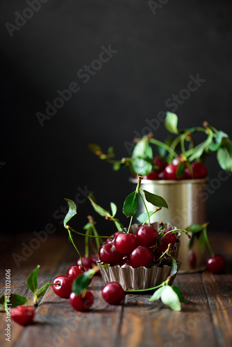 Close-up ripe red cherries against bowl with berries on brown wooden table. Soft focus