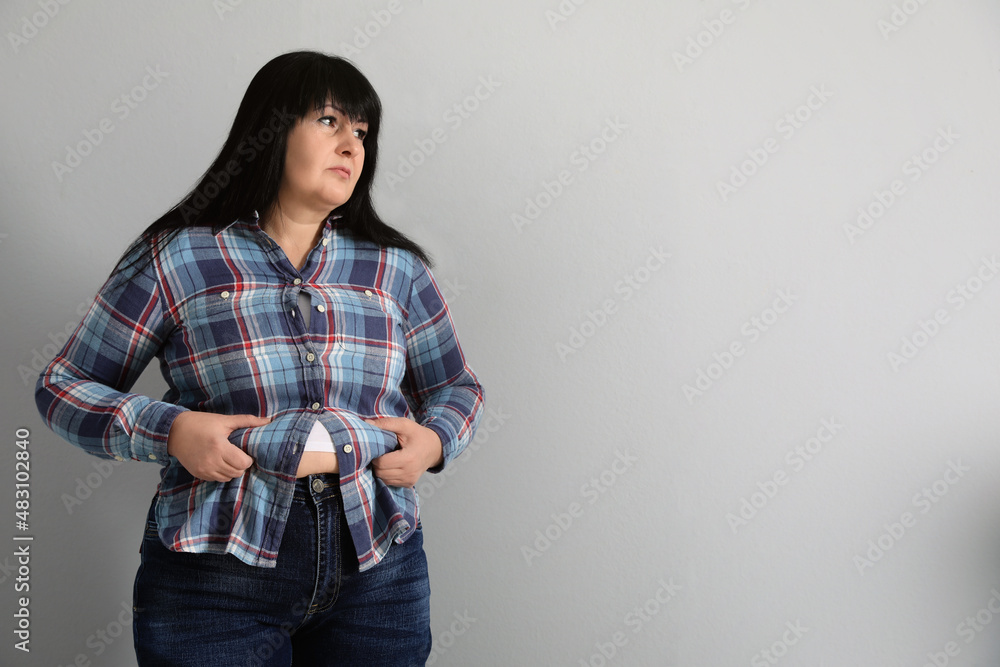 Overweight woman in tight shirt on light grey background. Space for text Overweight woman in tight shirt on light grey background. Space for text
