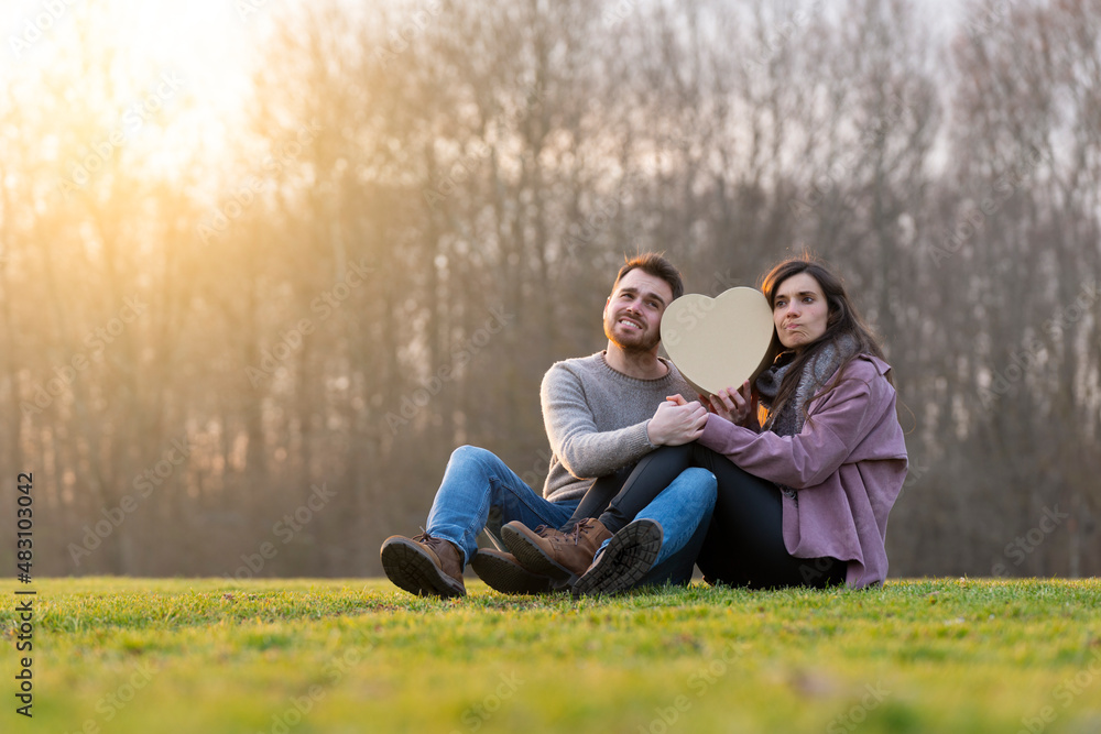 Young couple in love thinking about what might be inside a heart-shaped gift Young couple in love thinking about what might be inside a heart-shaped gift