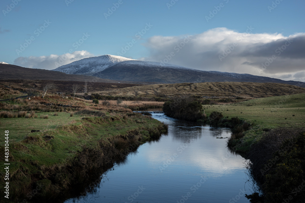 A river at the edge of Wild Nephin National Park in Ireland. Snow on the mountaintops of Wild Nephin Mountains. 