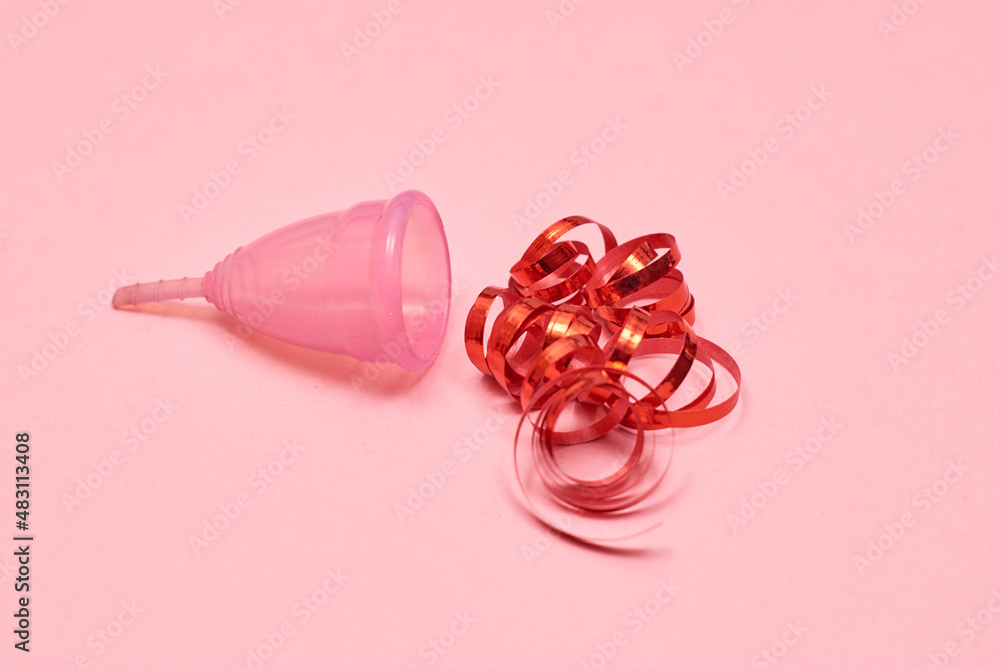 Pink menstrual cup on pink background. Decorated with red ribbon. Pink menstrual cup on pink background. Decorated with red ribbon.