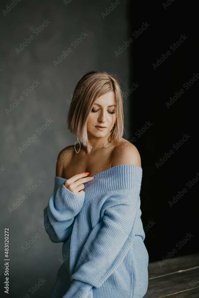 a blonde girl in a blue sweater and white sneakers is standing at the table a blonde girl in a blue sweater and white sneakers is standing at the table