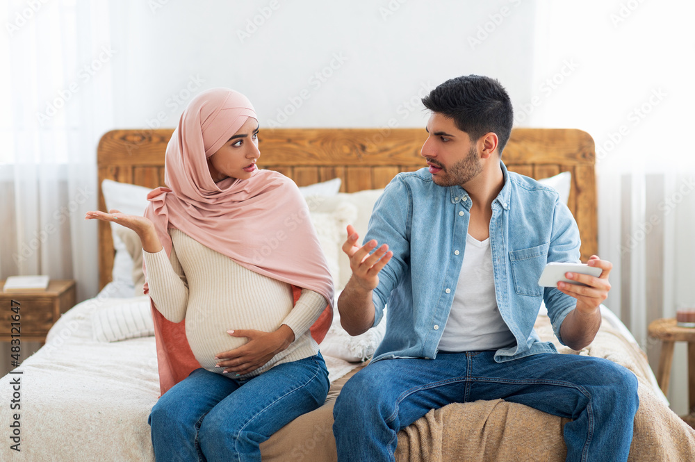 Pregnancy and relationship problems. Muslim couple arguing at home, expectant arab lady and her husband quarreling Pregnancy and relationship problems. Muslim couple arguing at home, expectant arab lady and her husband quarreling