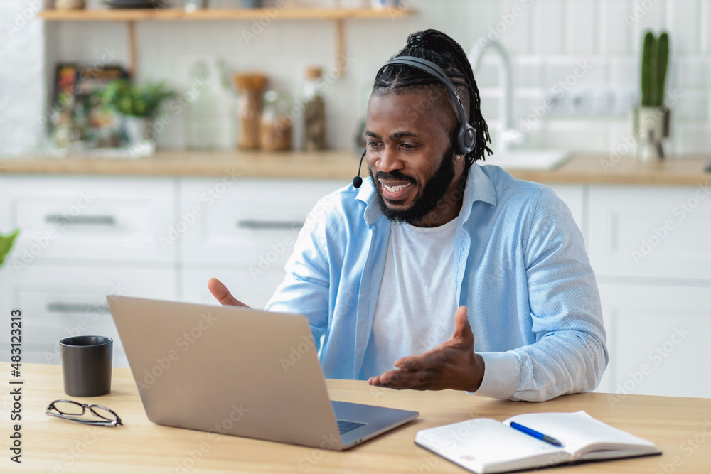 Smiling African American teacher man in headset teaching remotely at home using laptop computer, talking to students during a lecture, video call, e-learning concept Smiling African American teacher man in headset teaching remotely at home using laptop computer, talking to students during a lecture, video call, e-learning concept