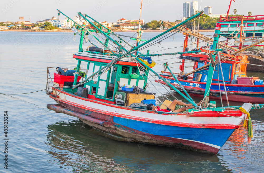 In the evening, colorful fishing boats are securely tied down directly at the pier with seaman's ropes and knots In the evening, colorful fishing boats are securely tied down directly at the pier with seaman's ropes and knots