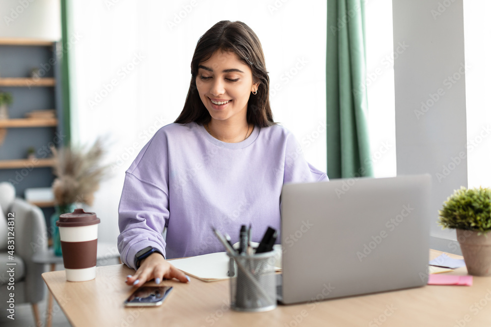 Cheerful lady sitting at table using cell and pc Cheerful lady sitting at table using cell and pc