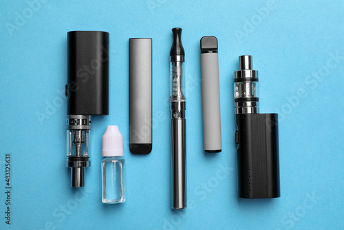 Different electronic cigarettes and liquid solution on light blue background, flat lay