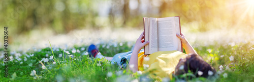 Small child lying down on the field in the spring park and reading a book photo