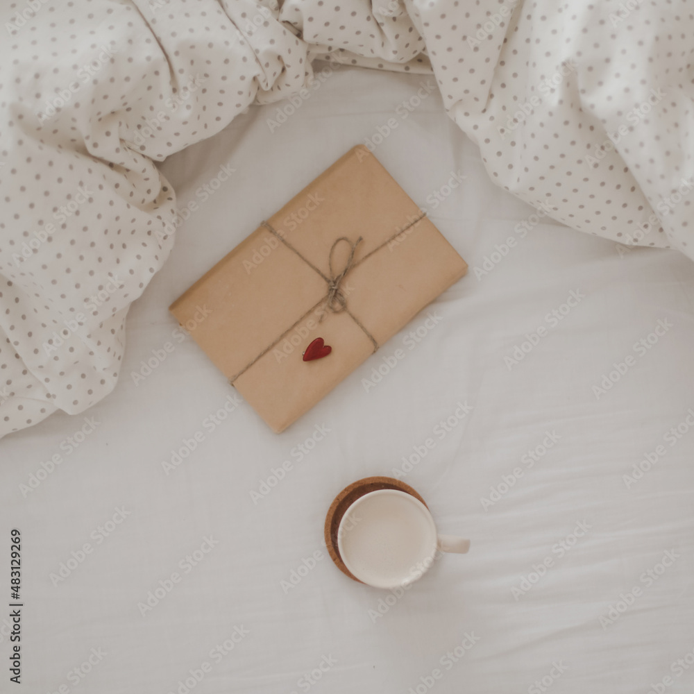 Cup of coffee and a gift on the bed with white linens and blanket. Morning coffee in bed concept. Cup of coffee and a gift on the bed with white linens and blanket. Morning coffee in bed concept.