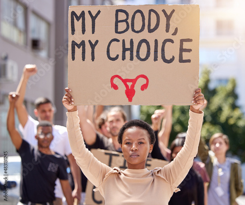 This is my body. Shot of a young woman at a rally holding a placard. © Anela R/peopleimages.com