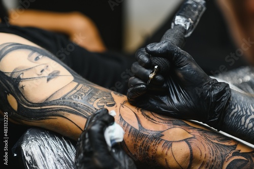 Tattoo salon. The tattoo master is tattooing a man. Tattoo machine, safety and hygiene at work. Close-up, tinted, tattooist. © Serhii