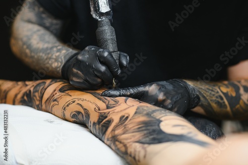 Tattoo salon. The tattoo master is tattooing a man. Tattoo machine, safety and hygiene at work. Close-up, tinted, tattooist. photo