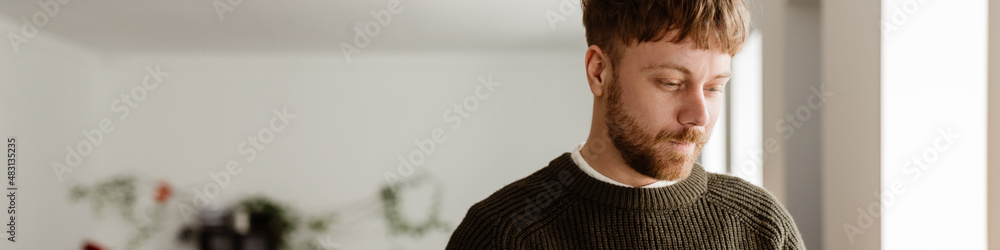 Fototapeta premium Young ginger man working with laptop while standing in office