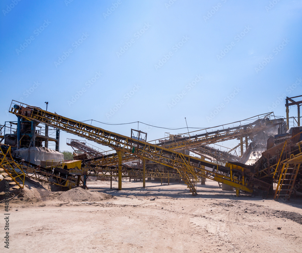 Crushing machinery, cone type stone crusher, conveying crushed granite gravel stone in a quarry open pit mining. Processing plant for crushed stone and gravel. Mining and Quarry mining equipment.