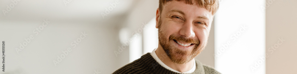 Obraz premium Young ginger man smiling and working with laptop while standing in office