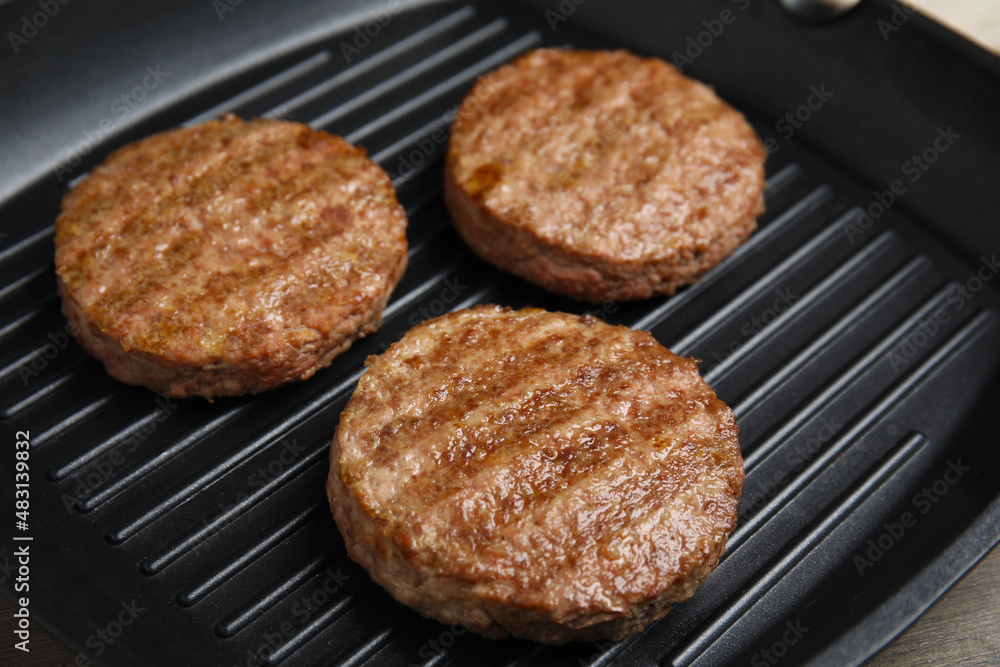Grill pan with tasty fried hamburger patties on wooden table, closeup