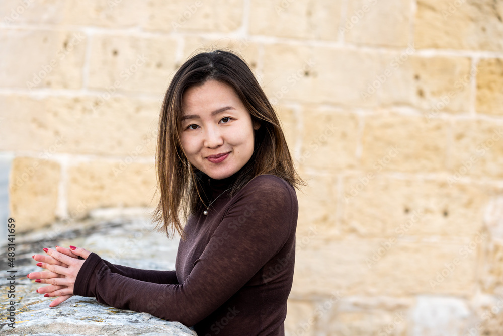 Portrait of a 29 year old Asian American girl standing on a fortress, hands folded
