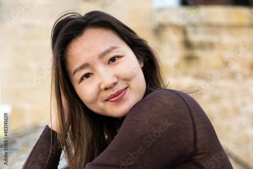 Portrait of a 29 year old Asian American woman, leaning on old stones, hands in the hair photo