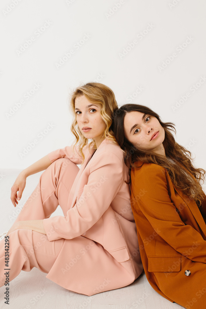 Modern young women in fashionable pastel suits with unbuttoned blazer sitting on a white background. Modern young women in fashionable pastel suits with unbuttoned blazer sitting on a white background.