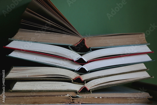 Stack of open vintage hardcover books on the shelf. Selective focus, green background.