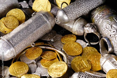 A lot of stacked gold bullion bars and gold coins and silver coins in a treasure sack. Treasure background. 
gold and silver jewelry. Ancient treasure. Pirate treasure and gold and silver filled crate