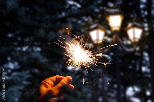 Hand holding sparkler firework firing with sky in background, concept of new year