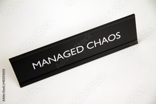 Managed Chaos, metal black and silver sign on a white shelf