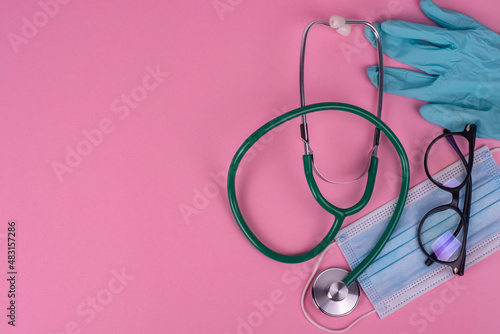Doctor's stethoscope, mask and gloves on a pink background.