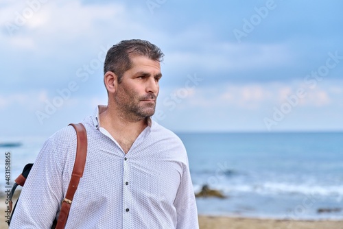 Outdoor portrait of mature man with backpack on seashore, copy space