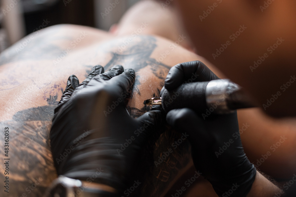 Professional male tattoo master in black gloves stuffs a tattoo on a male body in the studio, close-up. workflow of tattoo artist
