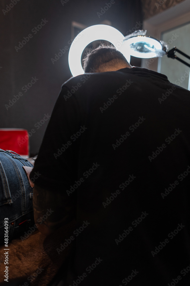 Professional tattoo artist makes a tattoo in a studio with light