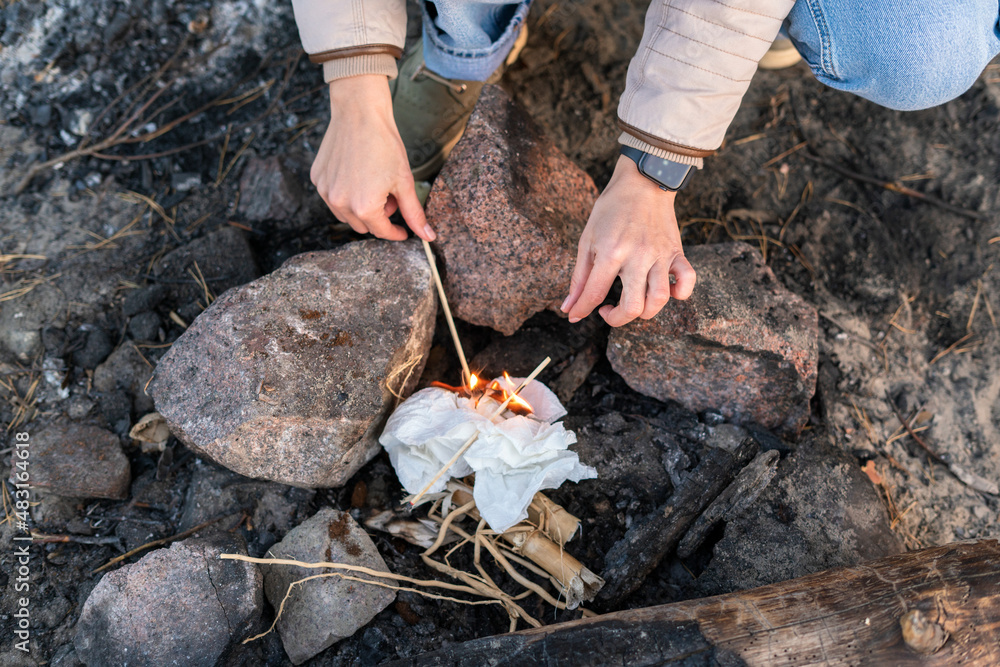 Cropped view of the caucasian woman making campfire while sitting near the rocks at the nature and holding dry sticks Cropped view of the caucasian woman making campfire while sitting near the rocks at the nature and holding dry sticks